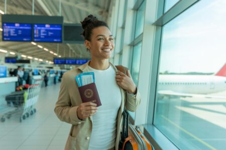 Viajante sorridente segurando passaporte e documento de seguro em aeroporto com aviões ao fundo.