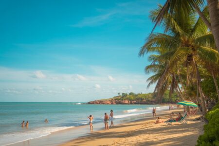 Praia tropical ensolarada em Porto Seguro com areia dourada, mar calmo e coqueiros ao vento, turistas aproveitando o dia.