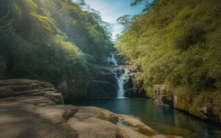 Cachoeira da Toca com água caindo de penhascos rochosos cercados por vegetação tropical densa e um lago azul cristalino abaixo.